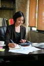 A beautiful Asian businesswoman calculates sales using a calculator and laptop Royalty Free Stock Photo
