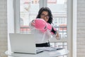 Businesswoman sitting at desk with laptop computer in office wearing boxing gloves