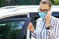 Beautiful successful prosperous rich business woman in white suit talking on phone wearing a medical mask standing near the car