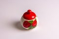 A beautiful sugar bowl with painted strawberries and a red lid, filled with white sugar on a white background