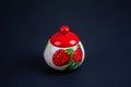 A beautiful sugar bowl with painted strawberries and a red lid, filled with white sugar on a black background