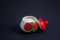 A beautiful sugar bowl with painted strawberries and a red lid, filled with white sugar on a black background