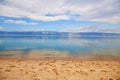 Beautiful summer background. Sandy beach, blue water, mountains in the background, cloudy sky. Lake Baikal Royalty Free Stock Photo