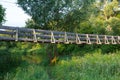 Beautiful summer day shot of an old narrow wooden hanging bridge over Nerl river with high green grass, vibrant vegetation, tall Royalty Free Stock Photo