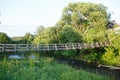 Beautiful summer day shot of an old narrow wooden hanging bridge over Nerl river with high green grass, vibrant vegetation, tall Royalty Free Stock Photo