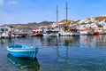 Beautiful summer day in typical marina of Greek island. Fishing boats, yachts by jetty. Whitewashed houses. Small boat