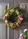 Beautiful summer flower wreath made of pink and white roses and lady`s mantle blossom hangs on old weathered wooden door. Royalty Free Stock Photo