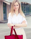 Beautiful summer Girl on the street with a big red super fashionable handbag in a White blouse and skirt on a warm evening.