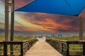 A beautiful summer landscape at the beach with a wooden footpath, people relaxing on the beach with colorful umbrellas, blue ocean