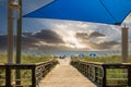 A beautiful summer landscape at the beach with a wooden footpath, people relaxing on the beach with colorful umbrellas, blue ocean