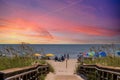 A beautiful summer landscape at the beach with a wooden footpath, people relaxing on the beach with colorful umbrellas, blue ocean