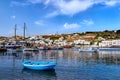 Beautiful summer in marina of Greek island. Fishing boats, yachts moored at jetty. Whitewashed houses. Small blue boat