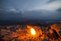 Beautiful summer night in mountain. Bright fire burns on rocky mountain top under blue cloudy sky. Royalty Free Stock Photo