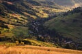 A beautiful summer rural landscape with houses, sunny hills and many small hay stacks. Carpathian rolling landscape on sunset in
