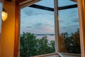 Beautiful summer sundown view from open window. Top of green trees on lake and cloudy sky background Royalty Free Stock Photo