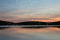 Stunning Summer sunset landscape of fireflies glowing above vibrant lake and hills in distance