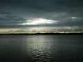 Beautiful Sun Rays of bright light shining through hole of dark clouds and illuminating lake water horizon in sunset time. Royalty Free Stock Photo