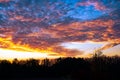 Magnificent evening sky with orange and violet clouds at sunset behind silhouettes of bare trees. Deep horizon. Royalty Free Stock Photo