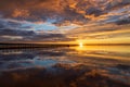 Beautiful sun setting over a wooden pier with puffy clouds blanketing the sky above.