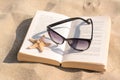 Beautiful sunglasses, book and starfish on sand Royalty Free Stock Photo