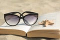 Beautiful sunglasses, book and starfish on sand, closeup Royalty Free Stock Photo