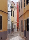 A beautiful sunlit narrow cobbled quiet street of old houses painted typical bright colors in ciutadella menorca Royalty Free Stock Photo