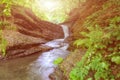 Beautiful sunny landscape with mountain waterfall in the rocky canyon surrounded be green forest Royalty Free Stock Photo