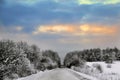 Beautiful sunrise behind clouds over a snowy country road. Royalty Free Stock Photo