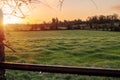 Beautiful sunrise in a country side. Simple rural area with green meadow and wooden fence for cattle. Sun glow in the background.