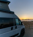 Beautiful sunrise with a gray camper van with a pop up roof parked at the beach