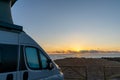 Beautiful sunrise with a gray camper van with a pop up roof parked at the beach