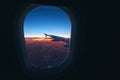 Beautiful sunrise view through the porthole during the flight. Plane wing above the cloudy colorful sunset Royalty Free Stock Photo