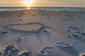 Beautiful sunset at the beach with wooden piles and hearts drawings in the sand Royalty Free Stock Photo