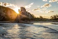 A beautiful sunset behind a hill on a beach with th image reflected on the sea shore.