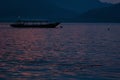 Beautiful sunset on calm sea with colorful saturated pink, purple smooth waves, dark blue mountains in distance, boat on horizon. Royalty Free Stock Photo