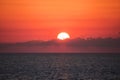 Beautiful sunset with deep red sky and clouds covering the glowing sun over the sea horizon Royalty Free Stock Photo