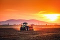 Beautiful sunset, farmer in tractor preparing land with seedbed