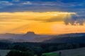 Beautiful sunset over countryside landscape of rolling hills with sun beams piercing sky and lighting hillside Royalty Free Stock Photo