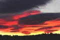 Beautiful sunset with red ribbon clouds like roses. Red-blue sunset over the city with dark clouds. Dark silhouette of the city