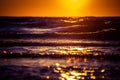 A beautiful sunset scenery with breaking waves close to the sandy shore. Sun shines in on the water surface. Royalty Free Stock Photo