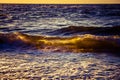 A beautiful sunset scenery with breaking waves close to the sandy shore. Sun shines in on the water surface. Royalty Free Stock Photo