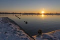 A beautiful sunset seen from a snowy boat dock where a line with buoys runs to an island with resting cormorants in lake Zoetermee