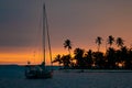 Beautiful sunset with silhouette of sailboat and palm trees on island. Vacation and adventure concept