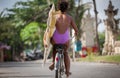 Beautiful surfer girl in purple bikini with afro hairstyle riding bicycle with one hand Royalty Free Stock Photo