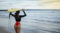 Beautiful surfer girl walking down to the beach for sunset surf session carrying blue - yellow surfboard on head with back in Royalty Free Stock Photo