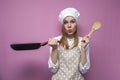 Surprised girl cook in kitchen clothes holds a frying pan and cooks dinner on a pink background, shocked woman housewife with Royalty Free Stock Photo