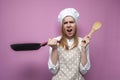 Surprised girl cook in kitchen clothes holds a frying pan and cooks dinner on a pink background, shocked woman housewife with Royalty Free Stock Photo