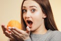 Beautiful surprised girl with long hair and orange, a young woman smiling and holding fruit near face on studio background, Royalty Free Stock Photo