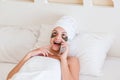 Beautiful surprised or shocked young woman with under eye patches and talking mobile phone in bathrobe lying in bed. Happy girl Royalty Free Stock Photo