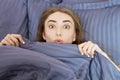 Beautiful surprised woman lying down in the bed after sleeping. Teen girl with open eyes with grey blanket. Morning concept. View